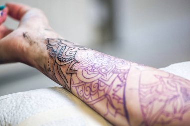Dövme ustası bir kızın eline siyah mürekkeple dövme yaptırıyor. Deri dövmesi.