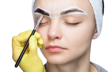 Makyöz, genç bir kızın kınasıyla kaşlarını boyuyor. Güzel kalın kaşlar yakın çekim. Profesyonel makyaj ve kozmetoloji cilt bakımı.