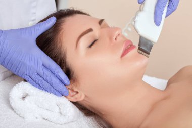 Kozmetik uzmanı güzellik salonundaki güzel bir kadının yüz derisinin ultrason temizleme işlemini yapıyor. Kozmetoloji ve profesyonel cilt bakımı.