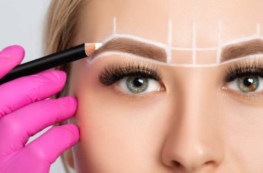 Woman Having Permanent Make-up Tattoo on her Eyebrows. Closeup beautician doing tattooing eyebrow. Green eyes close up. Professional makeup and cosmetology skin care. clipart