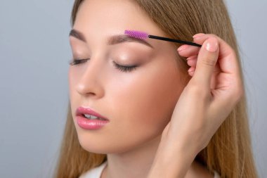 Makyöz, uzun saçlı, makyajlı, kalıcı makyajlı güzel bir genç kıza kaş taraması yapıyor. Makyaj konsepti, kaş şekli modeli..