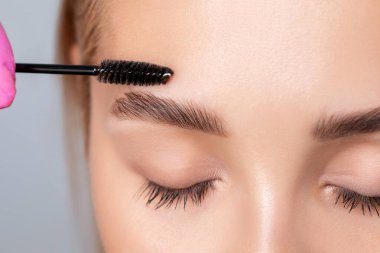 Makyöz, kalıcı makyajdan sonra temiz ciltli güzel sarışın bir kadına kaş tarıyor. Makyaj ve kozmetoloji konsepti, kaş şekli modelleme.