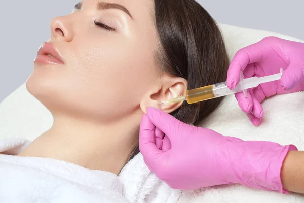 The doctor cosmetologist makes the injections procedure for smoothing wrinkles and against flabbiness of the skin on earlobe of a beautiful, young woman.Women\'s cosmetology in the beauty salon.