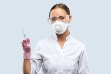 Beyaz önlüklü, maskeli, gözlüklü, lastik eldivenli bir doktor elinde aşı olan bir şırınga tutuyor. Tıbbi konsept, Covid-19.
