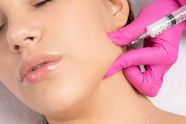 Kozmetik uzmanı, bir kadının çenesinde, yanaklarında ve boynunda çift çeneye karşı yağ yakmak için lipolitik enjeksiyon yapar. Güzellik salonunda kadın estetiği. Kozmetoloji konsepti..