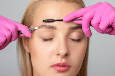 Makyöz, güzellik salonunu boyadıktan sonra kaşlarını tarar ve koparır. Profesyonel makyaj ve kozmetoloji cilt bakımı..