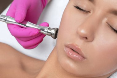 Kozmetik uzmanı, güzellik salonundaki güzel bir kızın yüzünün mikro cilt bakımını yapıyor. Kozmetoloji ve profesyonel cilt bakımı..