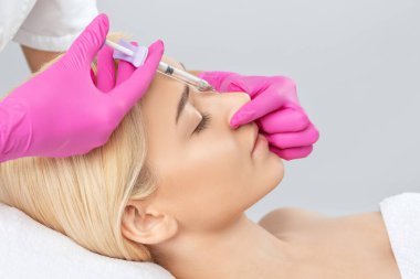 Doktor burundaki kamburu sarışının güzelliğiyle düzeltmek için iğne yapar. Güzellik uzmanı, yüzündeki kırışıklıklara karşı iğne yapar. Güzellik salonunda kadın kozmetolojisi.