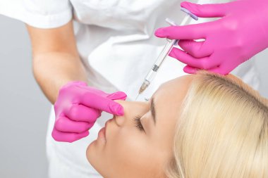 The doctor does injections to correct the hump on the nose with the beauty of the blonde. The beautician doees injections against wrinkles on the face. Women's cosmetology in a beauty salon. clipart