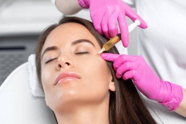 Cosmetologist does prp therapy on the face of a beautiful woman in a beauty salon. Women's cosmetology in the beauty salon. clipart