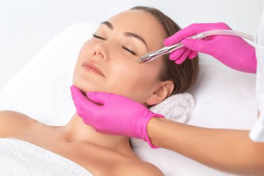 Kozmetik uzmanı yüzünde sivilce ve göz kenarındaki siyah noktalara karşı mikro dermabrüksiyon uygular. Güzellik salonunda kadın kozmetolojisi.