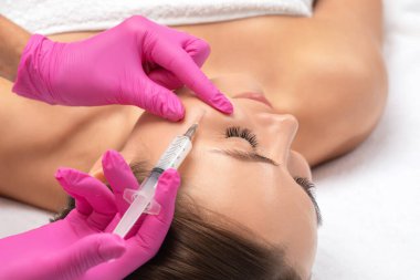 Kozmetik uzmanı, bir kadının çenesinde, yanaklarında ve boynunda çift çeneye karşı yağ yakmak için lipolitik enjeksiyon yapar. Güzellik salonunda kadın estetiği. Kozmetoloji konsepti..