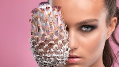 Gözler ve kaşlar kapanır. Güzel makyajlı ve sağlıklı ciltli güzel bir genç kızın portresi. Yüzün yanında çiçek var. Makyaj ve kozmetoloji kavramı.