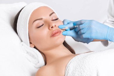 Kozmetik uzmanı, güzel bir kadının burun kıvrımlarında dudak büyütme ve kırışıklık önleyici iğneler yapar. Güzellik salonunda kadın kozmetolojisi.