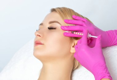 Kozmetik uzmanı güzel bir kadının yüzüne kırışıklık önleyici iğneler yapıyor. Güzellik salonunda kadın estetiği..