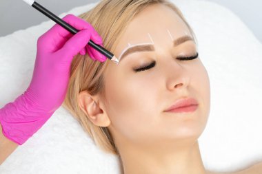Permanent make-up for eyebrows of beautiful woman with thick brows in beauty salon. Closeup beautician doing tattooing eyebrow. Professional makeup and cosmetology skin care.