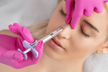 Doktor burundaki kamburu sarışının güzelliğiyle düzeltmek için iğne yapar. Güzellik uzmanı, yüzündeki kırışıklıklara karşı iğne yapar. Güzellik salonunda kadın kozmetolojisi.