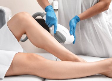 Bir kadının vücudunda Elos epilasyon tüy çıkarma prosedürü. Güzellik uzmanı bir güzellik salonunda bacağının alt kısmında lazer gençleştirme yapıyor. İstenmeyen vücut kılları alınıyor. Donanım ipl kozmetolojisi