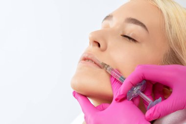 Kozmetik uzmanı, güzel bir kadının burun kıvrımlarında dudak büyütme ve kırışıklık önleyici iğneler yapar. Güzellik salonunda kadın kozmetolojisi.