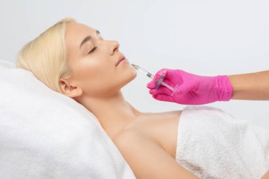Kozmetik uzmanı, güzel bir kadının burun kıvrımlarında dudak büyütme ve kırışıklık önleyici iğneler yapar. Güzellik salonunda kadın kozmetolojisi.
