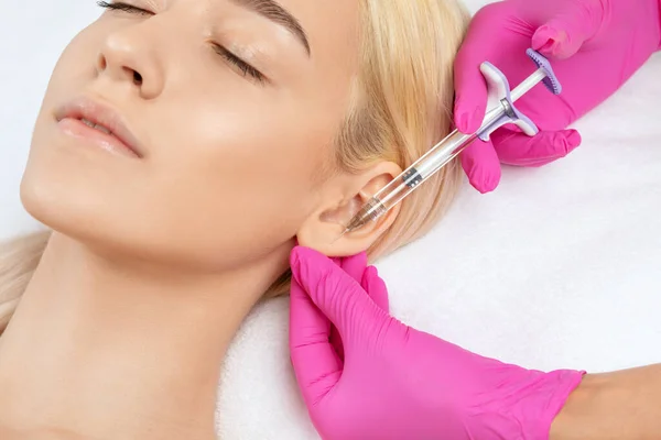 The doctor cosmetologist makes the injections procedure for smoothing wrinkles and against flabbiness of the skin on earlobe of a beautiful, young woman.Women's cosmetology in the beauty salon.