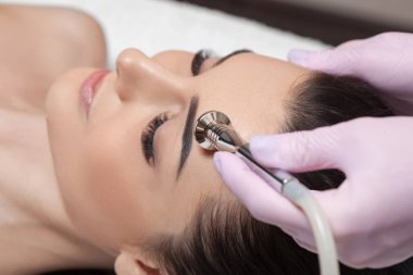 Kozmetik uzmanı, güzellik salonundaki güzel bir kızın yüzünün mikro cilt bakımını yapıyor. Kozmetoloji ve profesyonel cilt bakımı..