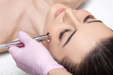 Kozmetik uzmanı, güzellik salonundaki güzel bir kızın yüzünün mikro cilt bakımını yapıyor. Kozmetoloji ve profesyonel cilt bakımı..
