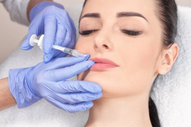 Kozmetik uzmanı, güzel bir kadının burun kıvrımlarında dudak büyütme ve kırışıklık önleyici iğneler yapar. Güzellik salonunda kadın kozmetolojisi.