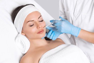 Kozmetik uzmanı, güzel bir kadının burun kıvrımlarında dudak büyütme ve kırışıklık önleyici iğneler yapar. Güzellik salonunda kadın kozmetolojisi.