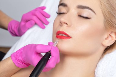 Güzellik salonundaki sarışın güzel kadının kırmızı dudakları için kalıcı makyaj. Dudak dövmesi yaptıran yakın güzellik uzmanı. Güzellik salonunda kadın estetiği..