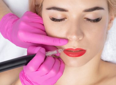 Güzellik salonundaki sarışın güzel kadının kırmızı dudakları için kalıcı makyaj. Dudak dövmesi yaptıran yakın güzellik uzmanı. Güzellik salonunda kadın estetiği..