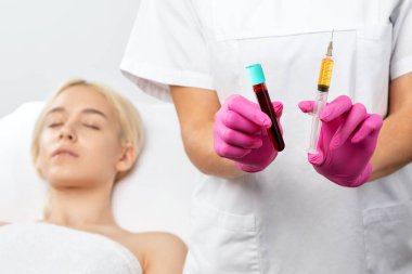 Güzellik uzmanı kırışıklıklara karşı uygulamalı tedavi uygulayacak. Enjeksiyon için kan plazması ve test tüpünde plazma olan bir şırınga var. Güzellik salonunda kozmetoloji.