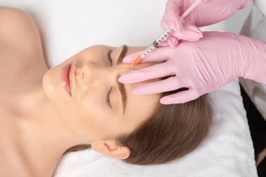 Kozmetik uzmanı güzel bir kadının yüzüne kırışıklık önleyici iğneler yapıyor. Güzellik salonunda kadın estetiği..