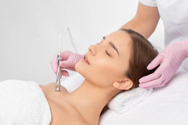 Kozmetik uzmanı, güzellik salonundaki güzel bir kızın yüz derisinin, boynunun ve köprücük kemiğinin mikro cilt bakımını yapıyor. Kozmetoloji ve profesyonel cilt bakımı..