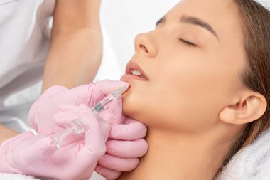 Kozmetik uzmanı, güzel bir kadının burun kıvrımlarında dudak büyütme ve kırışıklık önleyici iğneler yapar. Güzellik salonunda kadın kozmetolojisi.