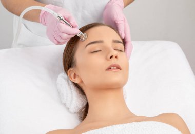 Kozmetik uzmanı, güzellik salonundaki güzel bir kızın yüzünün mikro cilt bakımını yapıyor. Kozmetoloji ve profesyonel cilt bakımı..