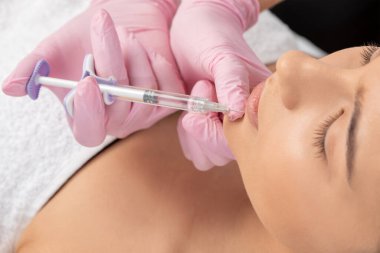 Kozmetik uzmanı, güzel bir kadının burun kıvrımlarında dudak büyütme ve kırışıklık önleyici iğneler yapar. Güzellik salonunda kadın kozmetolojisi.