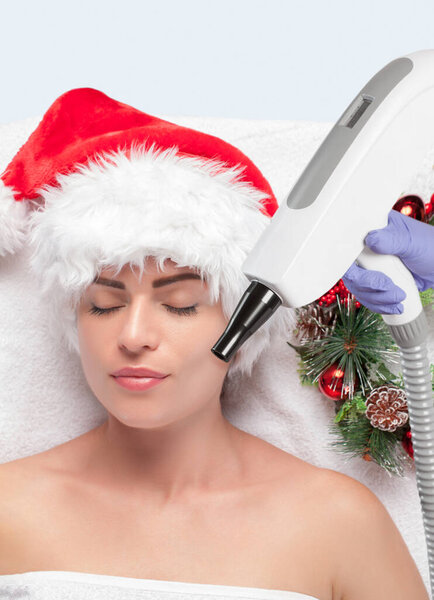 Carbon face peeling procedure in a beauty salon. Girl in santa claus hat. New Year's and Cosmetology concept.