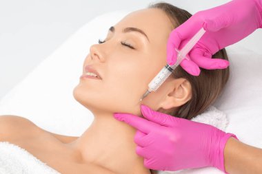 Kozmetik uzmanı, bir kadının çenesinde, yanaklarında ve boynunda çift çeneye karşı yağ yakmak için lipolitik enjeksiyon yapar. Güzellik salonunda kadın estetiği. Kozmetoloji konsepti..