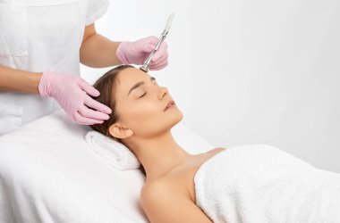 Kozmetik uzmanı, güzellik salonundaki güzel bir kızın yüzünün mikro cilt bakımını yapıyor. Kozmetoloji ve profesyonel cilt bakımı..