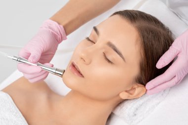 Kozmetik uzmanı, güzellik salonundaki güzel bir kızın yüzünün mikro cilt bakımını yapıyor. Kozmetoloji ve profesyonel cilt bakımı..