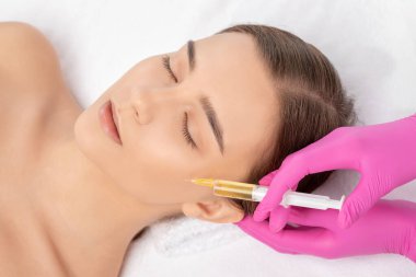 Kozmetik uzmanı güzellik salonunda güzel bir kadının yüzü üzerinde terapi uygular. Kozmetoloji kavramı.