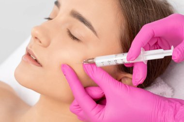 Kozmetik uzmanı, bir kadının çenesinde, yanaklarında ve boynunda çift çeneye karşı yağ yakmak için lipolitik enjeksiyon yapar. Güzellik salonunda kadın estetiği. Kozmetoloji konsepti..