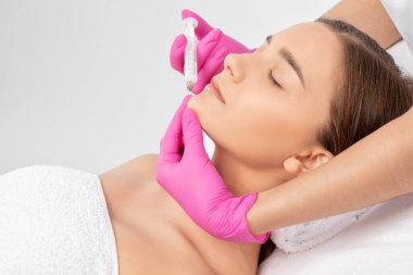 Kozmetik uzmanı, bir kadının çenesinde, yanaklarında ve boynunda çift çeneye karşı yağ yakmak için lipolitik enjeksiyon yapar. Güzellik salonunda kadın estetiği. Kozmetoloji konsepti..