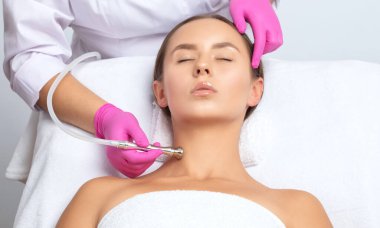 Kozmetik uzmanı, güzellik salonundaki güzel bir kızın yüz derisinin ve boynunun mikro cilt bakımını yapıyor. Kozmetoloji ve profesyonel cilt bakımı..