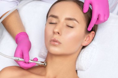 Kozmetik uzmanı, güzellik salonundaki güzel bir kızın yüz derisinin ve boynunun mikro cilt bakımını yapıyor. Kozmetoloji ve profesyonel cilt bakımı..