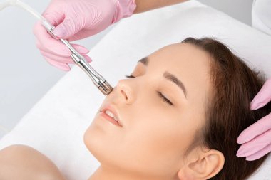 Kozmetik uzmanı, güzellik salonundaki güzel bir kızın yüzünün mikro cilt bakımını yapıyor. Kozmetoloji ve profesyonel cilt bakımı..