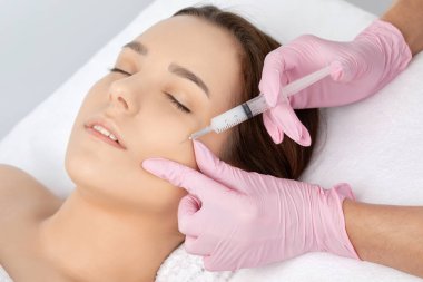 Kozmetik uzmanı, bir kadının çenesinde, yanaklarında ve boynunda çift çeneye karşı yağ yakmak için lipolitik enjeksiyon yapar. Güzellik salonunda kadın estetiği. Kozmetoloji konsepti..