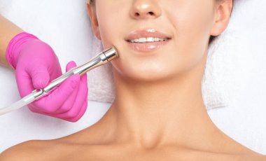 Kozmetik uzmanı, güzellik salonundaki güzel bir kızın yüz derisinin ve boynunun mikro cilt bakımını yapıyor. Kozmetoloji ve profesyonel cilt bakımı..