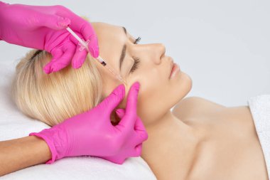 Kozmetik uzmanı güzel bir kadının yüzüne kırışıklık önleyici iğneler yapıyor. Güzellik salonunda kadın estetiği..